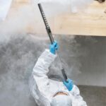 Overhead view of a person in safety gear fumigating a room, emitting white smoke for disinfection.