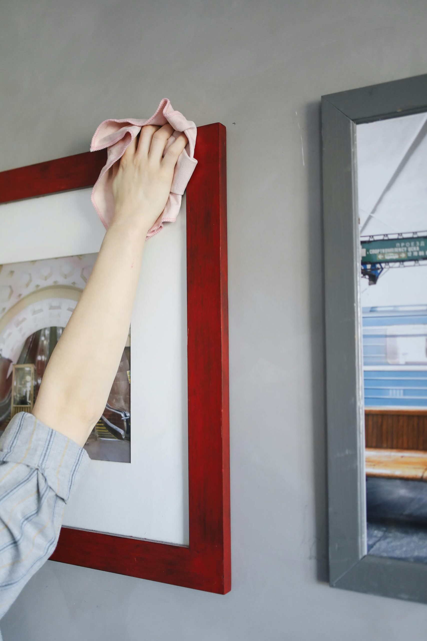 A person's hand cleaning a red picture frame in a well-lit indoor environment.